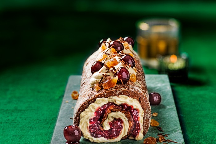 Chocolate, chestnut and cherry roulade A teal board topped with a chocolate roulade. The roulade is filled with cream and whole cherries