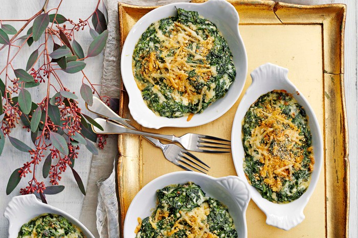 Steakhouse-Style Spinach Gratin Recipe Three white bowls filled with a green spinach gratin with melted cheese on top