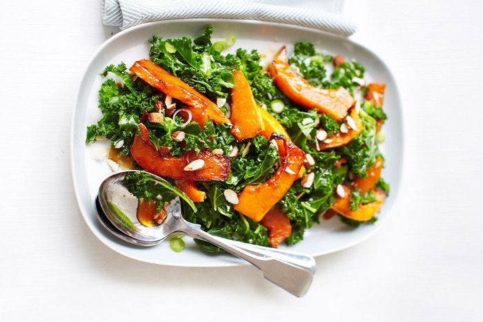 Kale salad with roasted butternut squash, pomegranate molasses and almonds Kale salad with roasted butternut squash, pomegranate molasses and almonds on a white plate with serving spoons