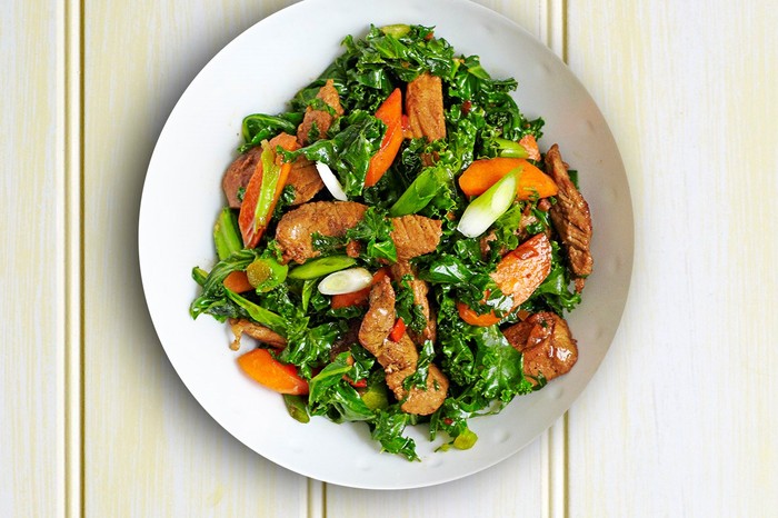 Pork, kale and spring onion stir-fry recipe Stir-fried kale, pork and carrots with chilli in a white bowl
