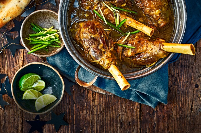 Lamb shank nihari A dish filled with lamb shanks in a deep brown curry broth with lime wedges on the side
