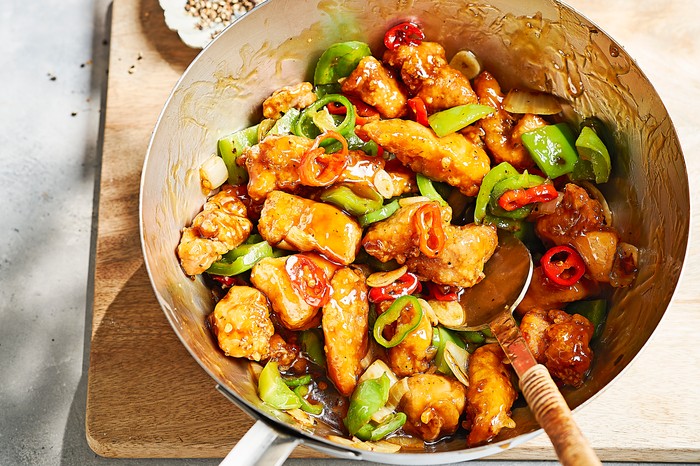 Easy Chilli Chicken Recipe Silver pan of chicken and chillies on a rustic wooden board