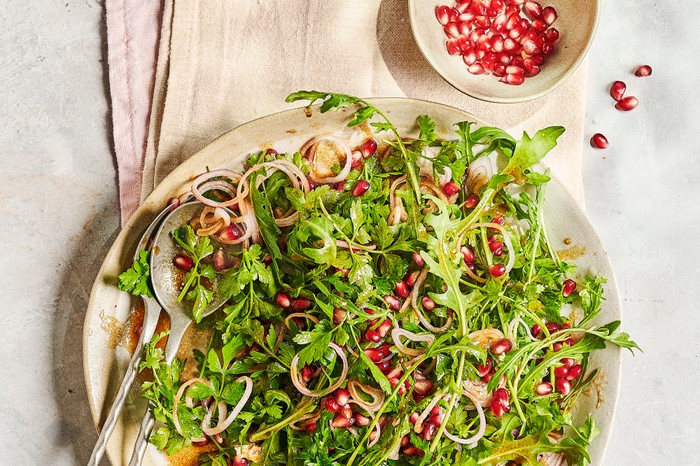 Parsley and Pomegranite Salad A round white serving plate of green leaves and red pomegranate seeds, sat on a folded piece of white linen