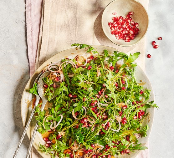 Parsley and Pomegranite Salad A round white serving plate of green leaves and red pomegranate seeds, sat on a folded piece of white linen