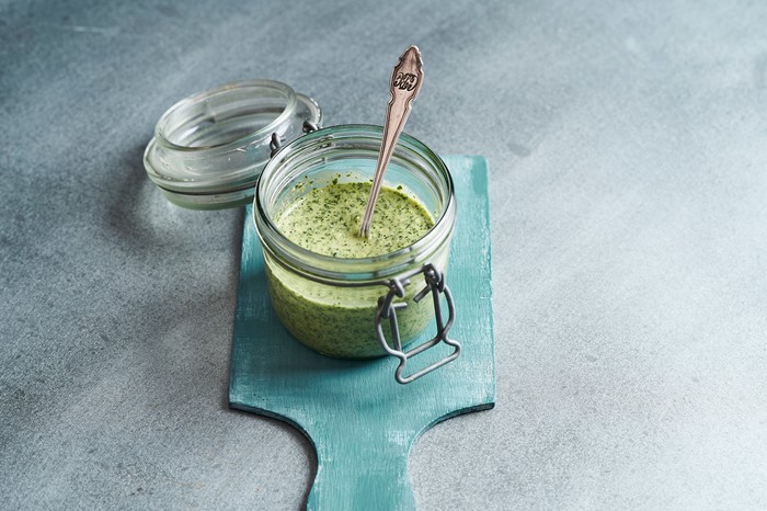 Kale pesto A grey background with a blue board, topped with a jar of green pesto sauce