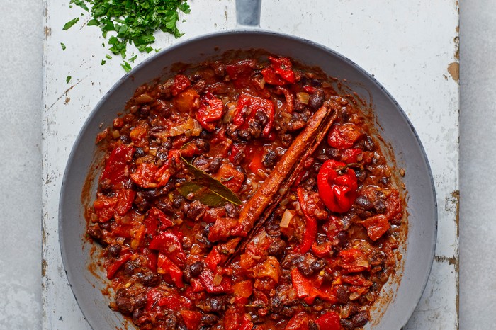 Caribbean-style black bean curry a silver pan with a wooden handle on a white wooden chopping board filled with pan of a bright-red coloured curry