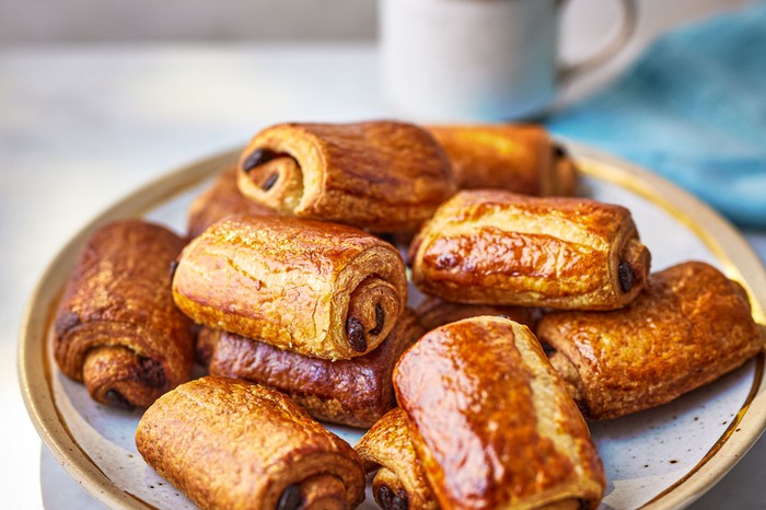 Pain Au Chocolat Recipe A plate of pain au chocolats with a mug of tea behind