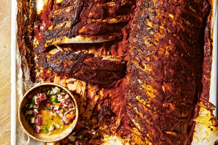 Pibil-style pork ribs two racks of pork ribs on baking parchment in a roasting tray with a pot of salsa