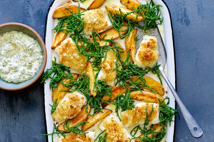 Fish and chips from JUST ONE PAN by Jane Lovett. Headline Home 2021. An oven tray filled with golden chunky chips and breadcrumbed hunks of fish on a blue background with a creamy dip