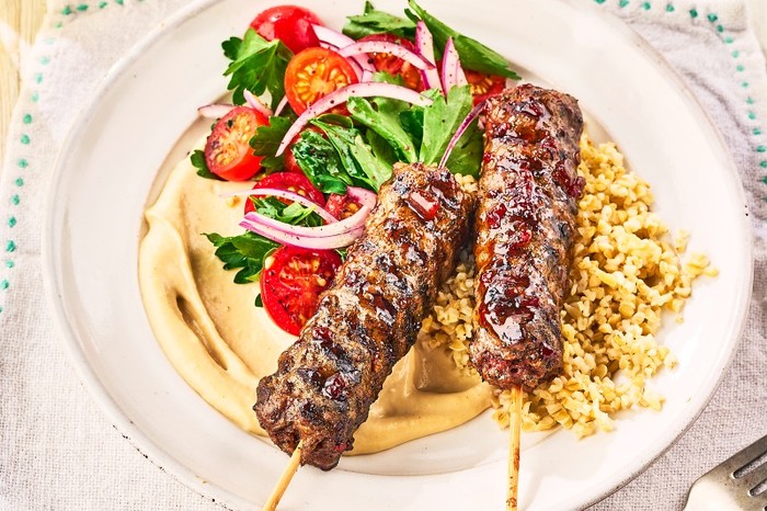 Pomegranate glazed lamb kebabs a plate of hummus, salad and lamb kebabs on wooden skewers