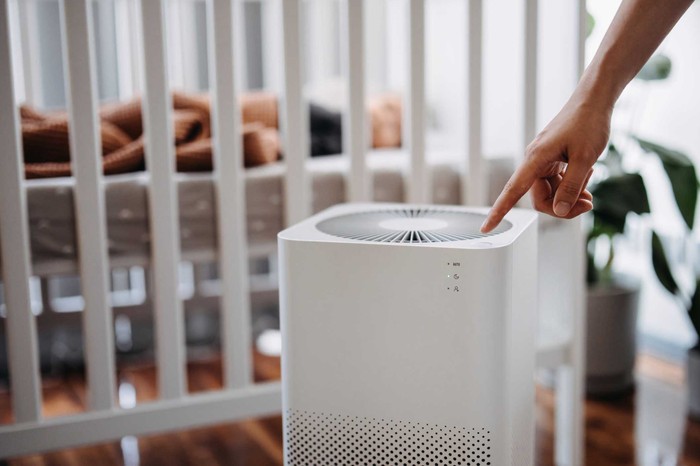 Close up hand of a mother turning on home air purifier for her newborn baby who is sleeping in the crib in the nursery. Fresh air. Cleaning and removing dust and bacteria. Healthier life and living concept