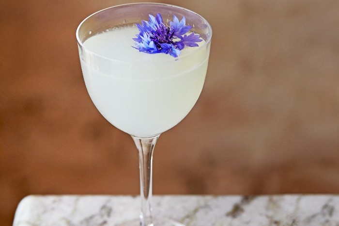 Bacalar A stemmed cocktail glass filled with an opaque white liquid topped with a purple flower