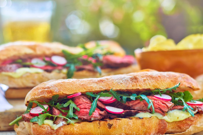 BBQ steak sandwich a sub-style sandwich packed with steak, rocket and radishes on a concrete surface outside