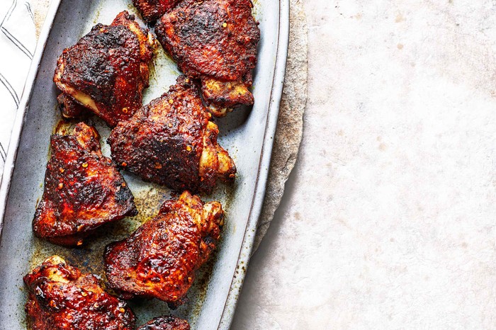BBQ Chicken Thighs Recipe With Ras El Hanout An oval platter topped with six BBQ chicken thighs with a red and blackened skin