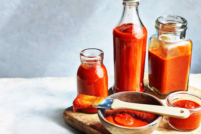 Homemade BBQ sauce Three glass bottles and a small wooden dish all filled with a vibrant red sauce