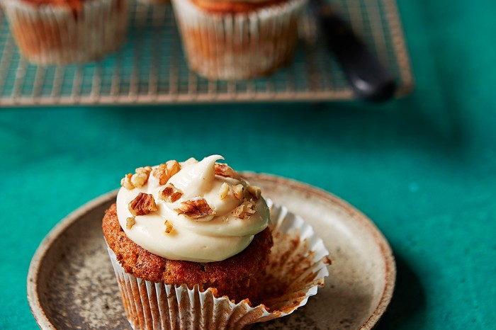 Carrot muffins with tahini buttercream A teal background topped with a small plate, with a golden muffin with white icing on top