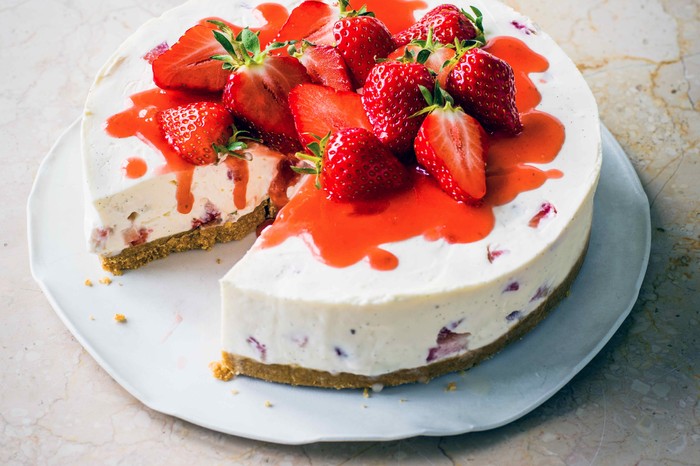 Strawberry Cheesecake Recipe A white cheesecake topped with red strawberries and whole strawberries on a white plate