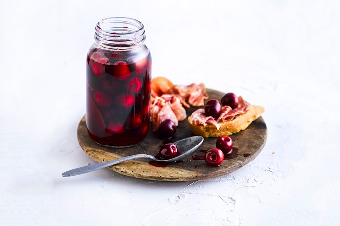 Pickled Cherries Recipe Pickled Cherries in a kilner jar served on a wooden board with ham and bread