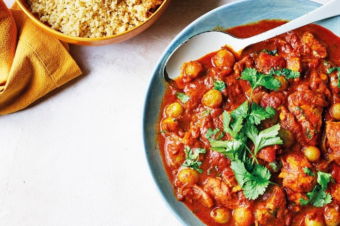 Chicken and gooseberry tagine a blue bowl filled with a red tagine with chunks of chicken and gooseberries next to a bowl of couscous