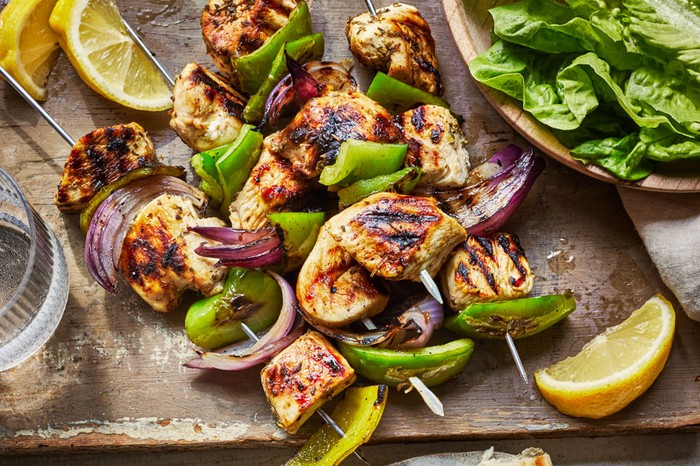 Chicken Souvlaki Recipe Chicken souvlaki skewers on a board, with a bowl of salad leaves on the side and two torn grilled pitta breads