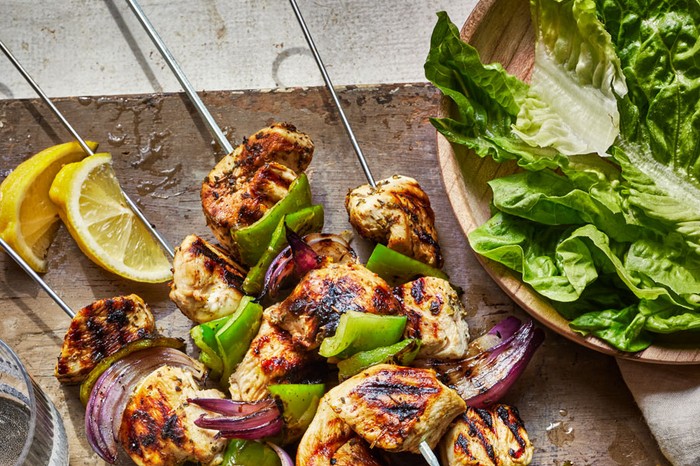 Chicken Souvlaki Recipe Chicken souvlaki skewers on a board, with a bowl of salad leaves on the side and two torn grilled pitta breads