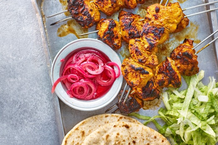 Chicken tikka A tray of golden spiced chicken pieces on metal skewers with a bowl of pink pickled onions