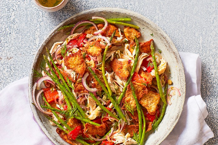 Roast chicken and asparagus panzanella A plate of chicken, asparagus and red peppers on a white cloth with a speckled grey background