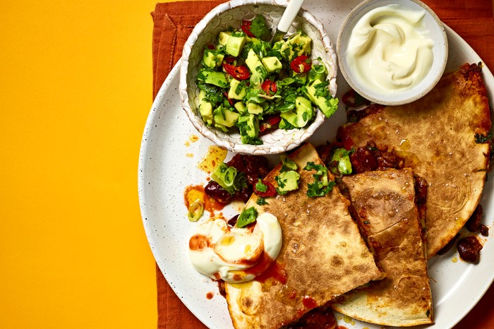 Chilli Con Carne Quesadillas a white plate of quesadillas, guag and sour cream on a red cloth with an orange background
