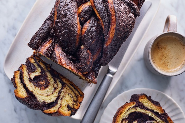 Chocolate babka Loaf marble cake on a plate with a slice cut out and a slice on a circular plate next to a tea