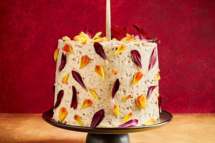 Chocolate celebration cake Chocolate and olive oil sponge cake decorated in hazelnut praline and edible flowers on a stand with a candle