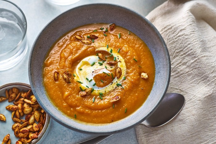 butternut squash soup a dark grey bowl filled with orange soup with a swirl of yoghurt and toasted pumpkin seeds