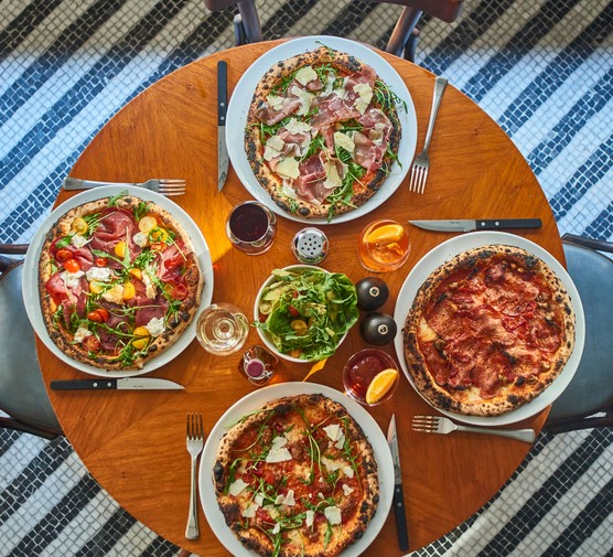 16 Best Italian Restaurants London Selection of pizzas at Cecconi's Pizza Bar, Soho A mahogany table is topped with four pizzas and glasses of Aperol spritz at Soho House's Cecconi's Pizza Bar