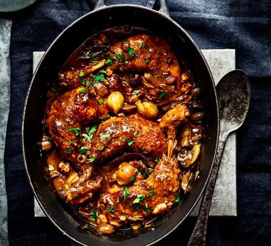 Coq au vin A black oval casserole pot with a serving spoon, filled with coq au vin and topped with parsley
