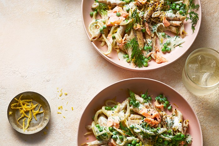 Creamy salmon and pea pasta Two bowls of salmon and pea pasta with lemon zest on the side