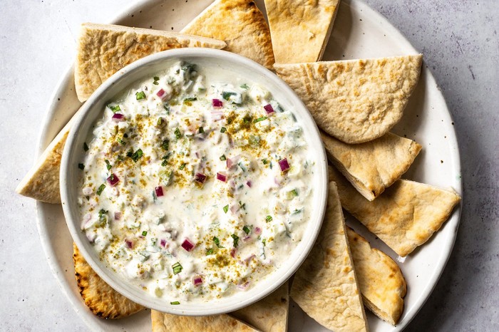 Cucumber Raita Recipe A small white bowl of dip with torn bread on the side
