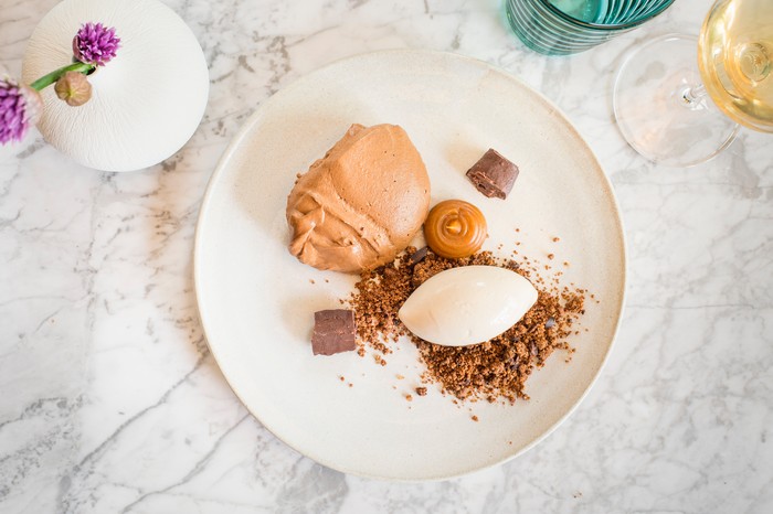 Pump Street Chocolate Mousse at Darby's Restaurant Battersea A white plate against a marble background. On the plate is a pale chocolate mousse with a scoop of ice cream and crumble biscuit base