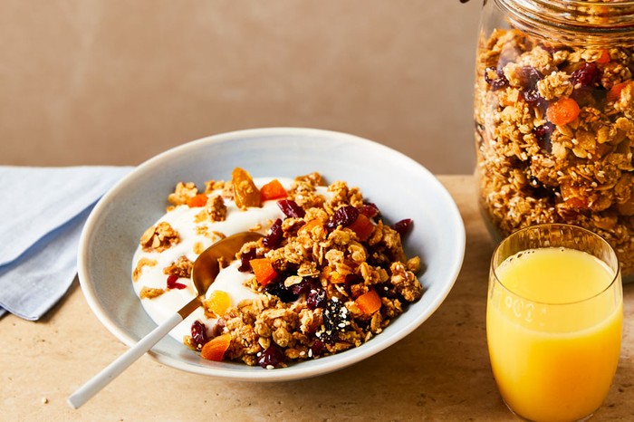 Granola Recipe A bowl of granola next to a jar of granola and a glass of orange juice