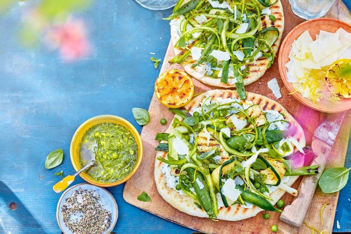 Vegetarian BBQ flatbreads flatbreads spread with ricotta and topped with ricotta and green veg on a wooden board
