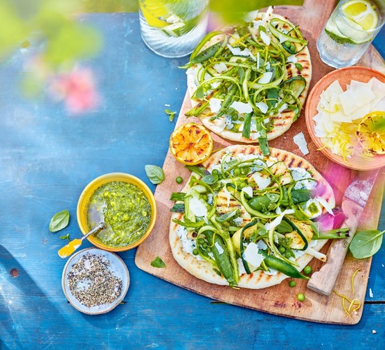 Vegetarian BBQ flatbreads flatbreads spread with ricotta and topped with ricotta and green veg on a wooden board
