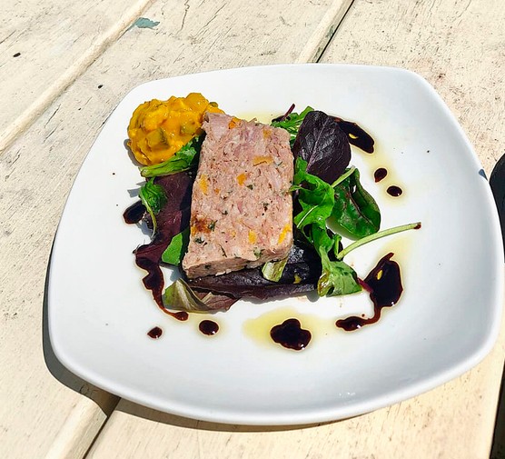 Ham hock terrine A white plate of ham hock terrine with salad leaves on a wooden garden table in the sun