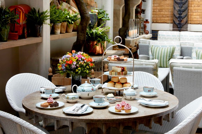 Ham Yard Hotel Afternoon Tea A table laid out for afternoon tea at Ham Yard Hotel including a three tiered cake stand, a blue and white tea pot and three blue and white tea cups and saucers, with flowers in pots in the background
