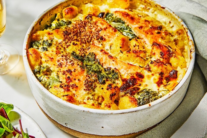 Hot smoked salmon, gnocchi spinach bake A deep dish filled with a golden topped bake with a linen napkin and glass of white wine