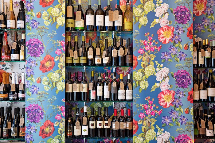 Interiors at Passione Vino Wine Bar, London A colourful room has floral-patterned wallpaper. Between the wallpaper is a section with bottles of wine