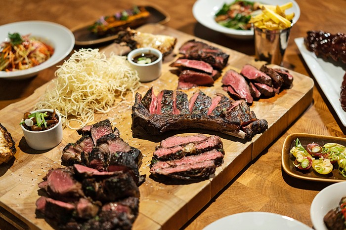 Block Soho Large cuts of meat on a wooden plank with side dishes such as chips