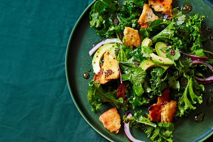 Kale salad with tadka dressing A green plate filled with kale, chopped avocado and golden croutons