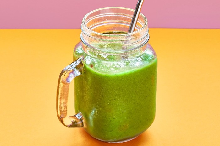 Kale smoothie A glass filled with green kale smoothie with a metal straw on an orange and pink background