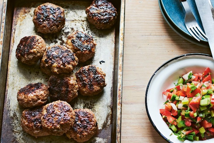 Lamb and beef kebabs with burnt aubergine A silver oven tray of round beef and lamb patties next to a chopped salad