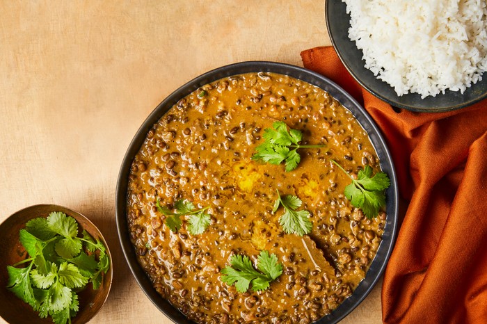 Langarwali dhal Brown lentil dhal in a bowl with coriander on top next to a bowl of rice