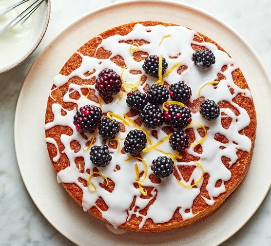 Lemon blackberry cake A sponge cake topped with splattered icing sugar and a scattering of blackberries on a white plate