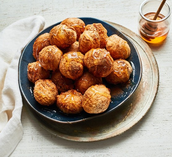 Loukoumades (Greek doughnuts) A black bowl of Loukoumades next to a glass pot of honey